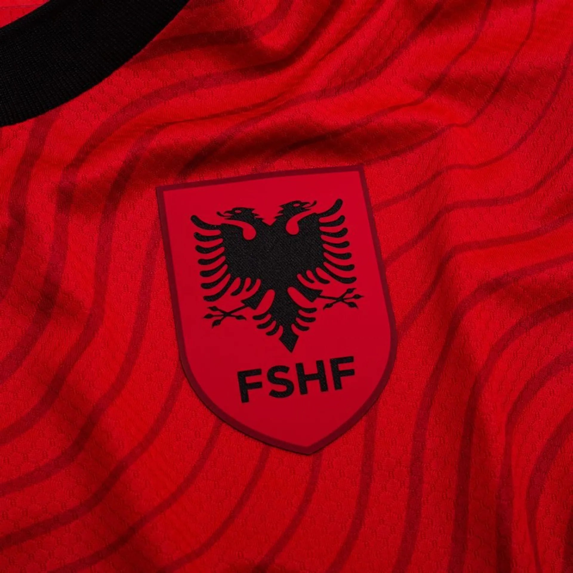 03c918ed4aab | UAE SPORT STORE Close-up of a red jersey with a shield crest showing a black double-headed eagle and the letters FSHF, representing the Albanian football association.