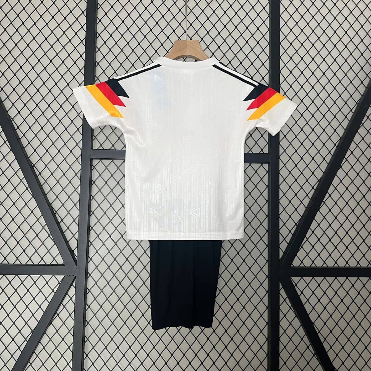 White short-sleeve shirt on a hanger, back view, with colorful angled shoulder accents in yellow, red, and black. Black pants hang below.