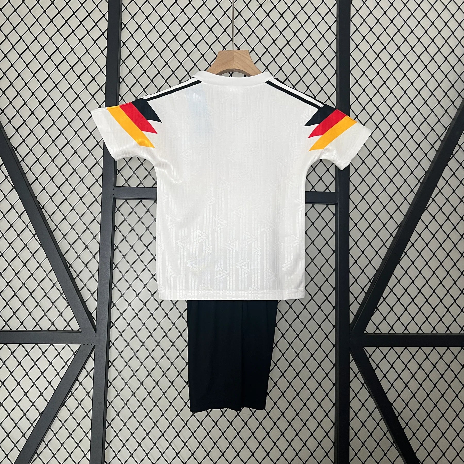 03f11bb0 | UAE SPORT STORE White short-sleeve shirt on a hanger, back view, with colorful angled shoulder accents in yellow, red, and black. Black pants hang below.