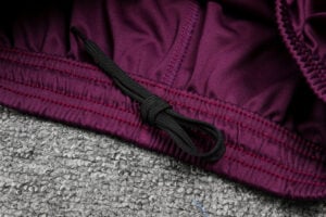 Close-up of a purple fabric waistband with a black drawstring tied in a knot on a gray textured surface