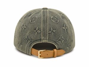 Back view of a denim baseball cap with an all-over monogram print and a tan leather strap with a gold buckle closure.