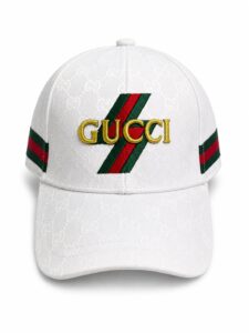 White Gucci baseball cap with gold embroidered 'GUCCI' logo over red and green diagonal stripes; monogram pattern all over the fabric and matching stripes at the sides.