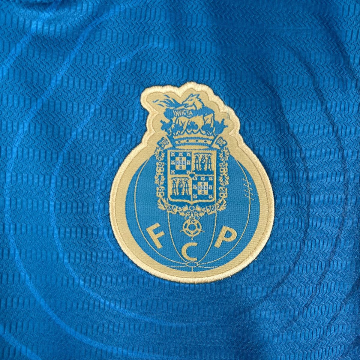 Close-up of a beige shield-shaped patch with a crest and an eagle sewn onto blue textured fabric.
