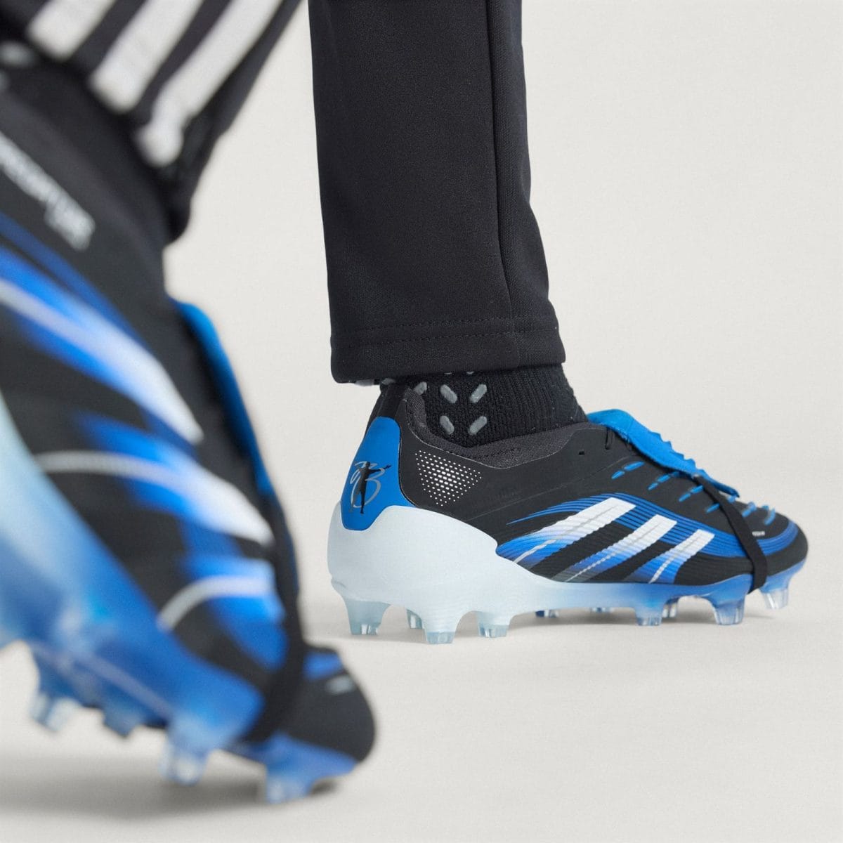 Close-up of blue and black soccer cleat with studded sole, worn with a black sock and pants leg visible above the shoe.
