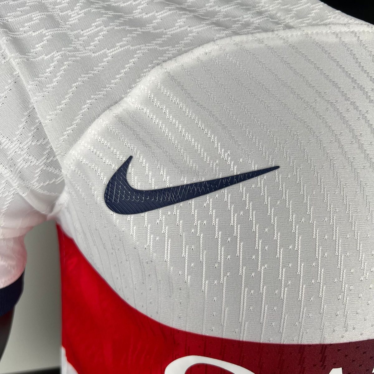 Dark navy Nike swoosh logo on white textured fabric with a red background nearby, cropped close-up.