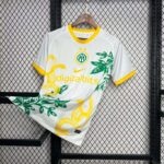White jersey with yellow trim on a wooden hanger, featuring green leaf graphics against a black metal grid display background.