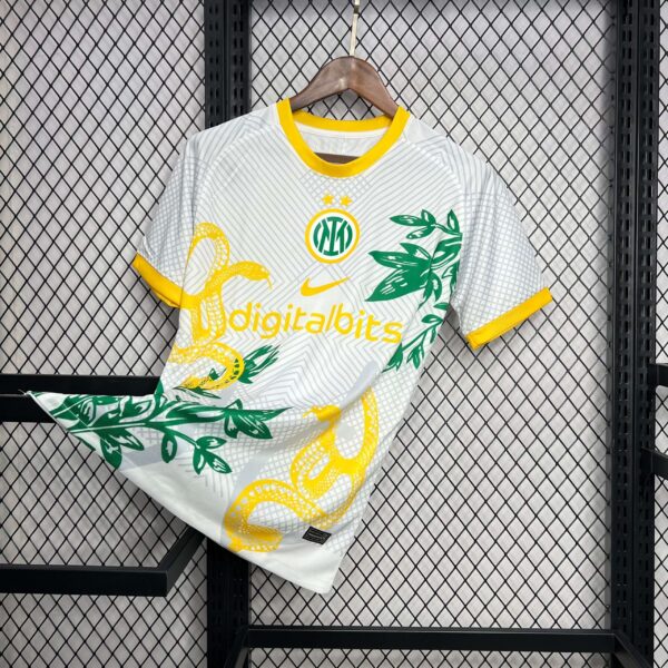 White jersey with yellow trim on a wooden hanger, featuring green leaf graphics against a black metal grid display background.