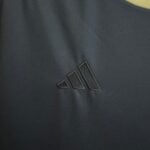 Close-up of dark fabric with visible diagonal weave and black stitched geometric patches near a yellow edge.
