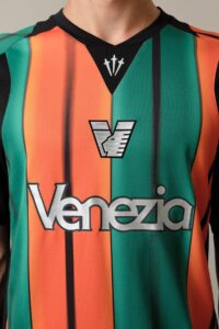 Close-up of a person wearing a green and orange Venezia football jersey with the club crest and sponsor text visible on the chest.