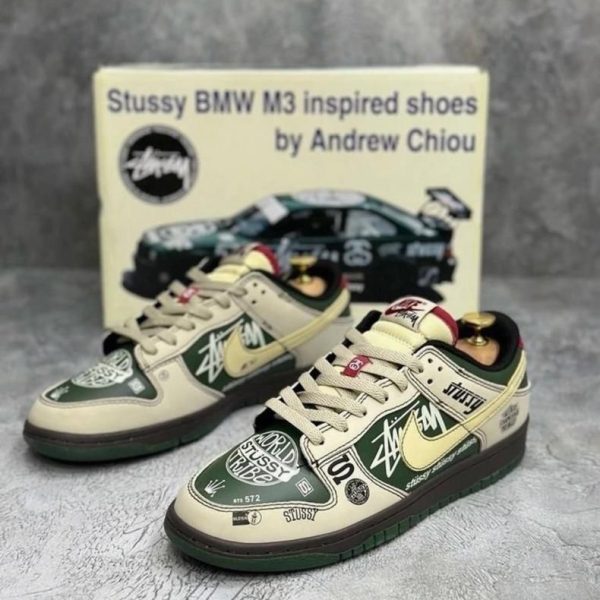 Pair of Stussy x BMW M3 inspired sneakers in cream and dark green with white and black graphic panels, placed in front of the product box.