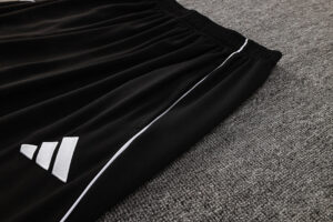 Black athletic pants with a white side stripe and Adidas logo on a gray carpet surface.