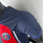 Close-up of a blue patterned bag with a red strap and Paris Saint-Germain crest badge.