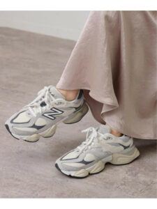 Pair of white and gray chunky sneakers peeking from a light pink dress on a pale floor.