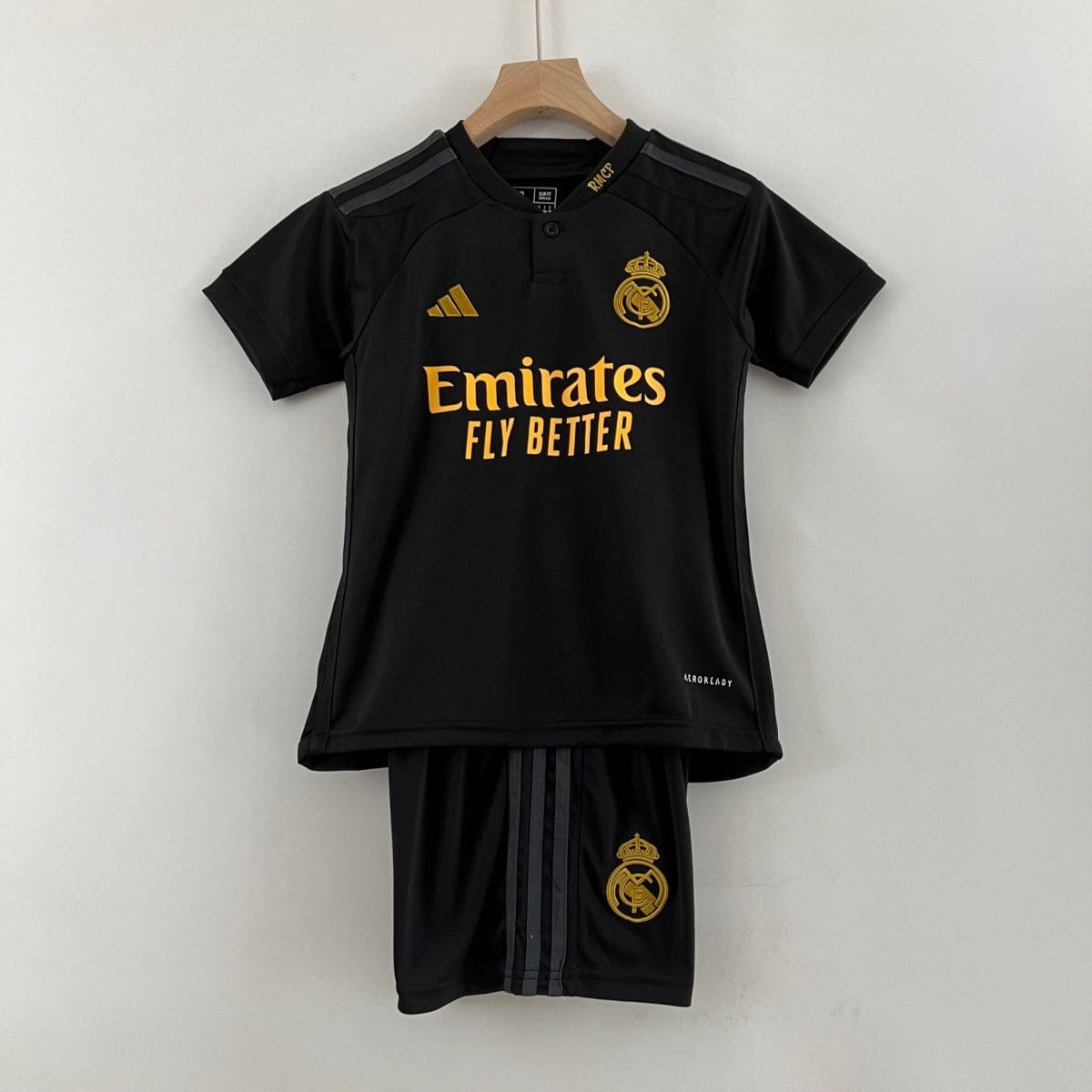 Black Real Madrid football jersey on a wooden hanger with gold crest and sponsor text Emirates Fly Better visible.
