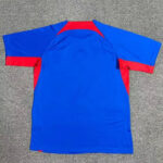 Blue athletic jersey with red trim on sleeves and back, viewed from the back on a gray surface.