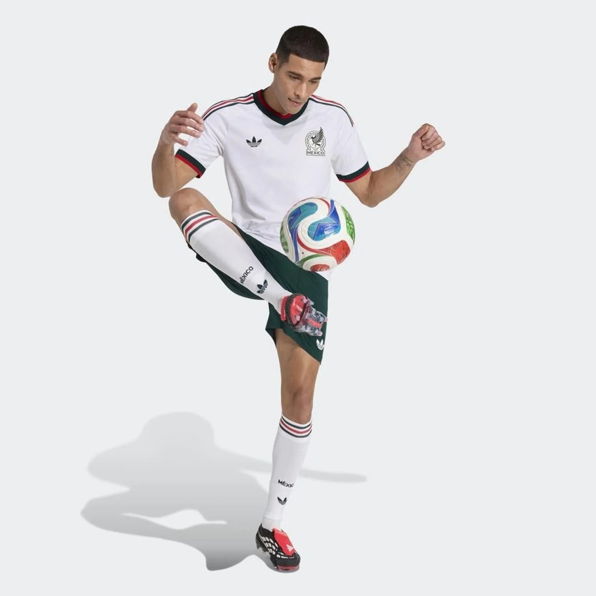 Male soccer player in a white Mexico jersey mid-kick, kicking a colorful soccer ball against a light background.