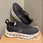 Black knit-on shoe with white cloud sole and On logo on the side, pair resting on a box.