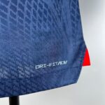 Close-up of blue patterned fabric on a seat with a red strap visible along the edge and a dark chair leg in the lower left corner.