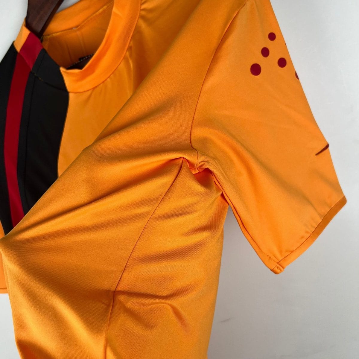 Close-up of bright orange fabric with a folded sleeve and small burgundy dots near the shoulder edge.