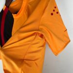 Close-up of bright orange fabric with a folded sleeve and small burgundy dots near the shoulder edge.
