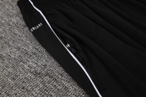 Close-up of black athletic pants with white piping and a zipper pocket on a gray carpet.