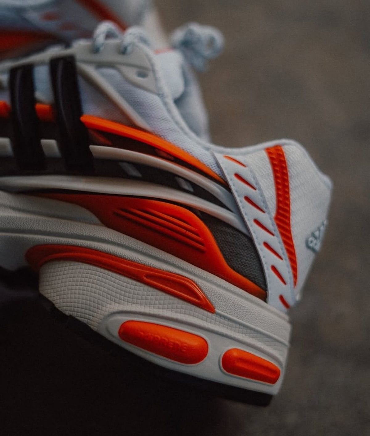 Close-up of a white running shoe with bright orange accents and a textured sole.