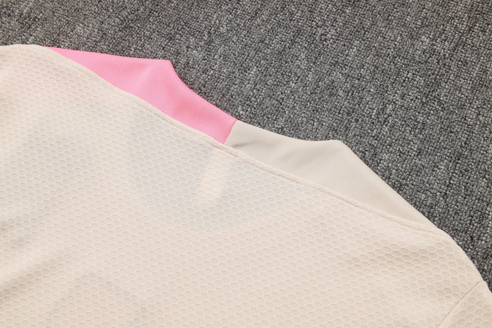 08c2c98b | UAE SPORT STORE Beige textured fabric with pink trim on a gray carpet background.
