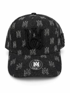 Black baseball cap with an all-over gray AMIRI monogram pattern and a large black embroidered logo on the front; curved brim and side strap detail with AMIRI badge on the brim