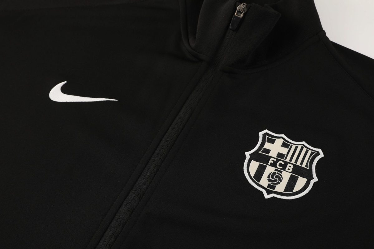 Close-up of a black jacket showing a white Nike swoosh and an FC Barcelona patch/crest near the zipper area.