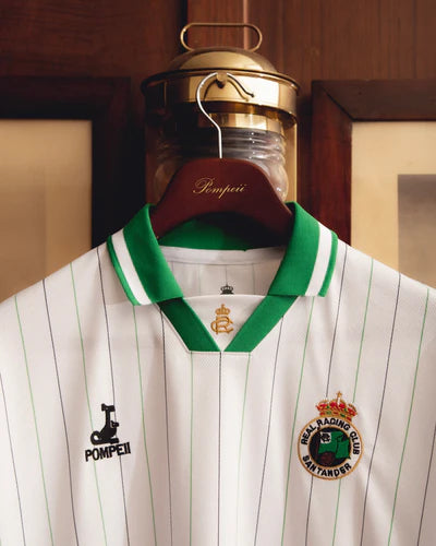 08web_400x_78e0bd58-3272-4272-9a2c-4f056d5fabb8 | UAE SPORT STORE White pinstripe polo jersey with a green collar hanging on a wooden hanger; left chest crest of a club, with a small black 'Pompei' logo on the opposite chest.