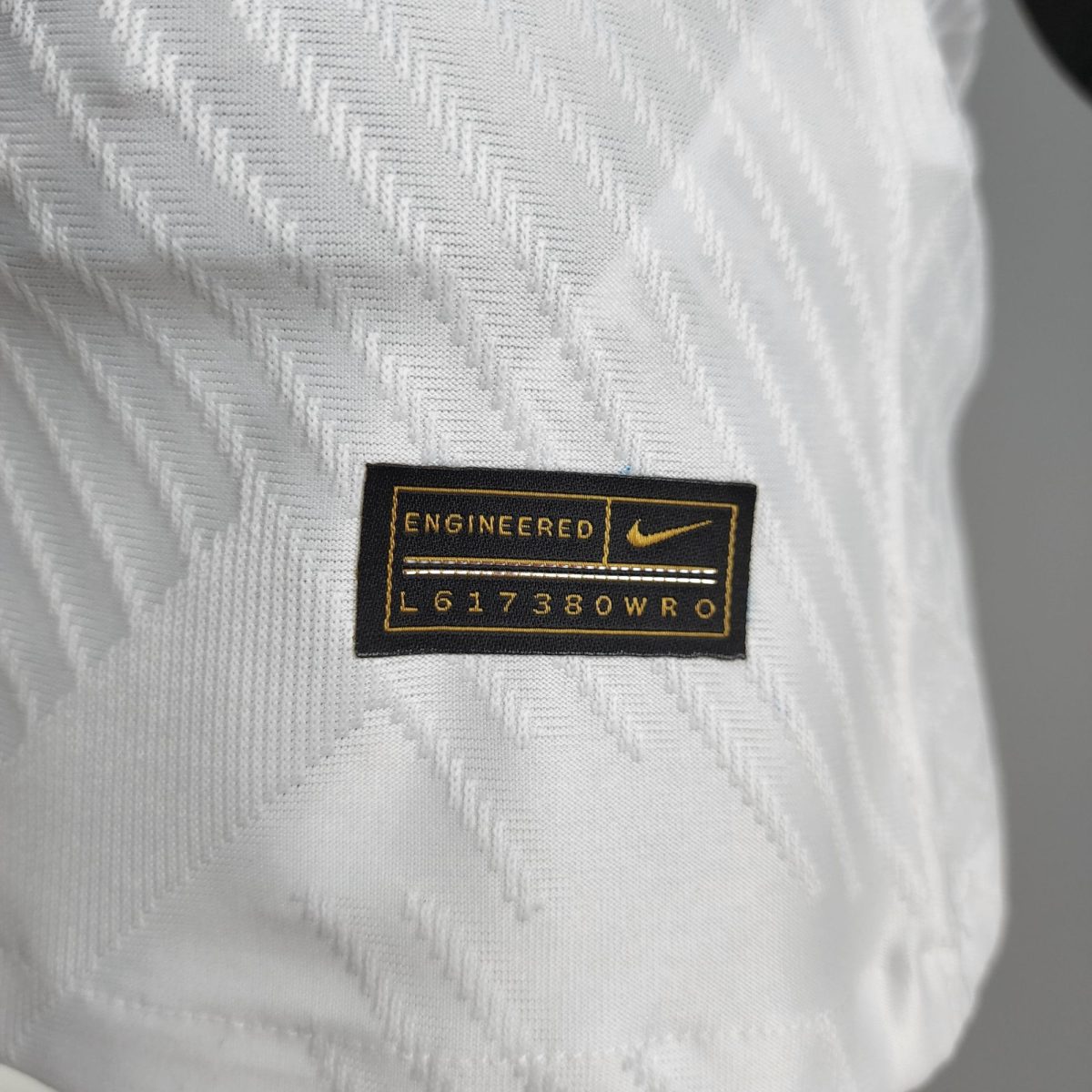 Close-up of white textured fabric with a black patch label reading 'ENGINEERED' and a small yellow Nike swoosh nearby.