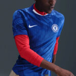 Person wearing a blue Chelsea FC jersey with a white Nike swoosh and crest, red long-sleeve undershirt showing at the arms.