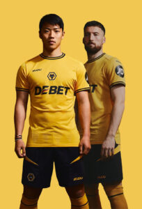 Two male soccer players in yellow kits stand side by side against a solid yellow background, facing forward.