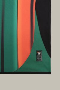 Close-up of green, orange, and black fabric panels on a sports jersey with Venezia FC and NOCTA badge.
