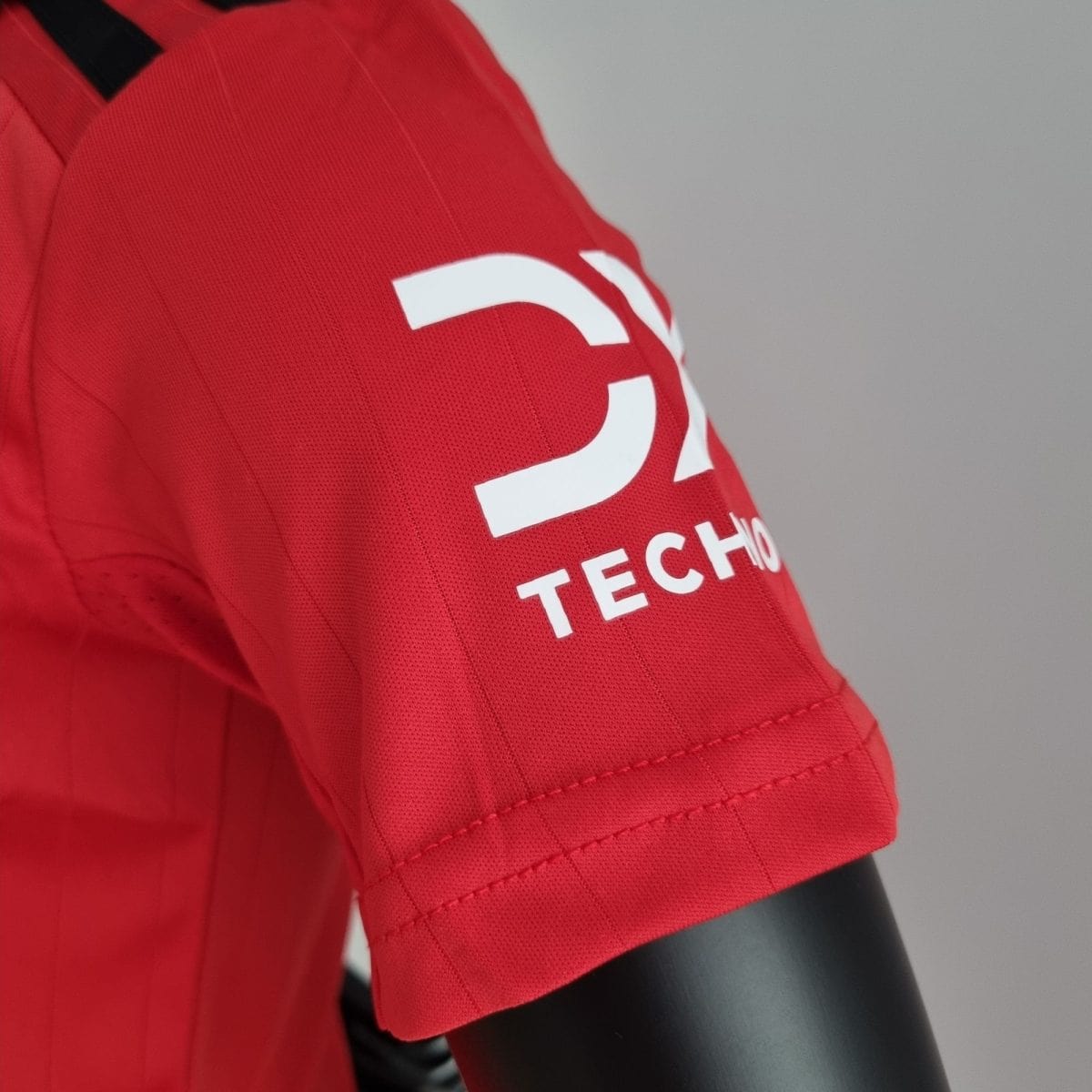 Close-up of a red athletic jersey sleeve with white lettering on a gray background.