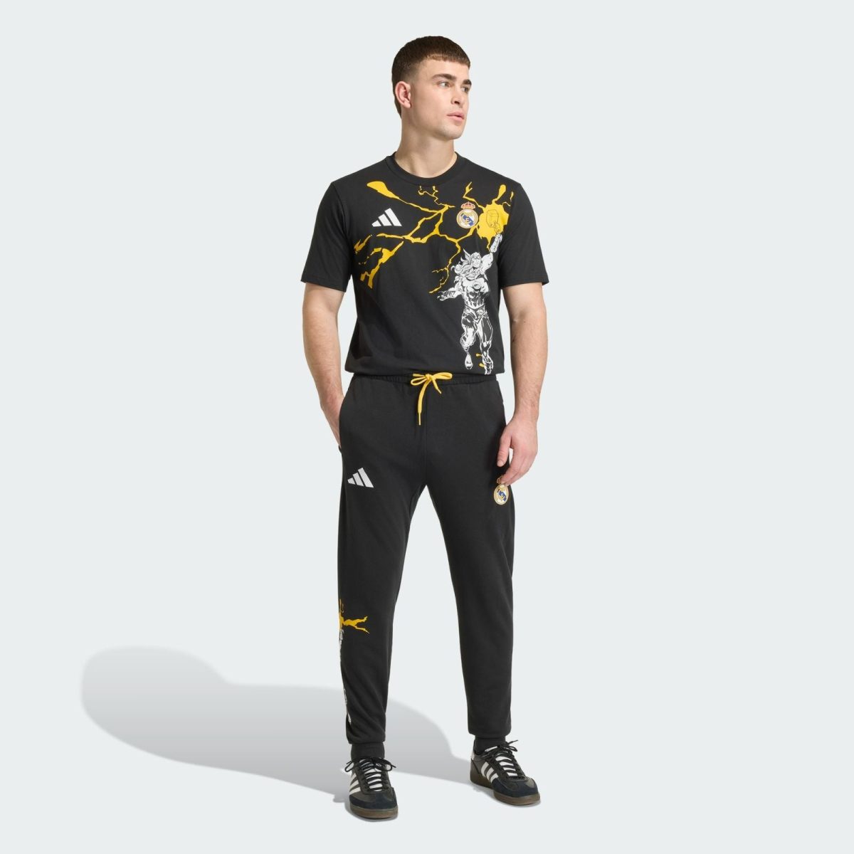 Man standing in a black Real Madrid training outfit with yellow lightning graphics and branding logos (Adidas and Real Madrid crest).