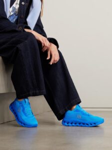 Person sitting on a step in dark denim jeans, wearing bright blue athletic shoes.