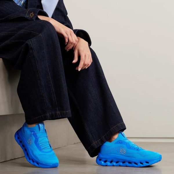 Person sitting on a step in dark denim jeans, wearing bright blue athletic shoes.