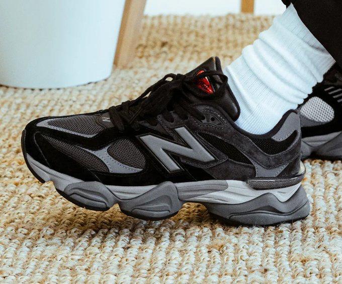 Black and gray New Balance sneaker resting on a textured beige carpet with a white sock nearby