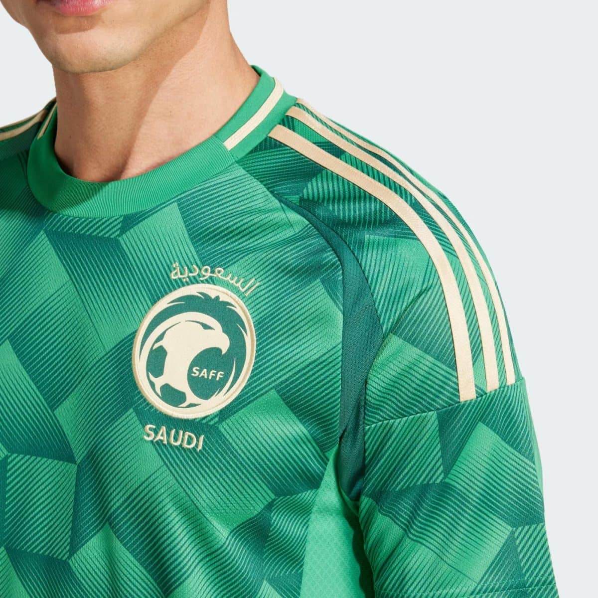 Close-up of a green Saudi national team jersey showing the crest and shoulder stripes.