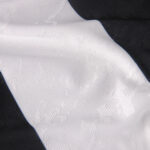 Close-up of white jacquard fabric with subtle geometric patterns draped over dark fabric.