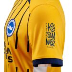 Close-up of a yellow soccer jersey sleeve with the Brighton & Hove Albion crest and blue sponsor text.