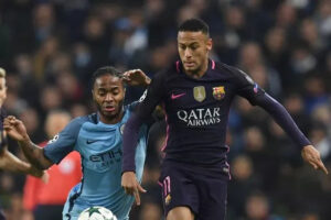 0_GettyImages-620133208 | UAE SPORT STORE Two footballers chase the ball during a match, one in Barcelona’s dark purple kit and the other in Manchester City’s light blue kit.
