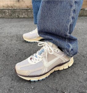 Cream-colored running shoes with white laces and mesh panels, worn with cuffed blue jeans on a paved surface.