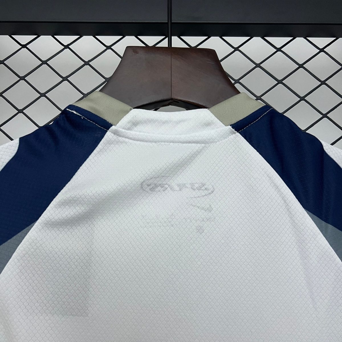 Wooden hanger supporting a navy and white garment against a metal chain-link fence.