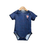 Navy blue baby onesie with pink speckles hanging on a wooden hanger, featuring a rooster emblem on the left chest.