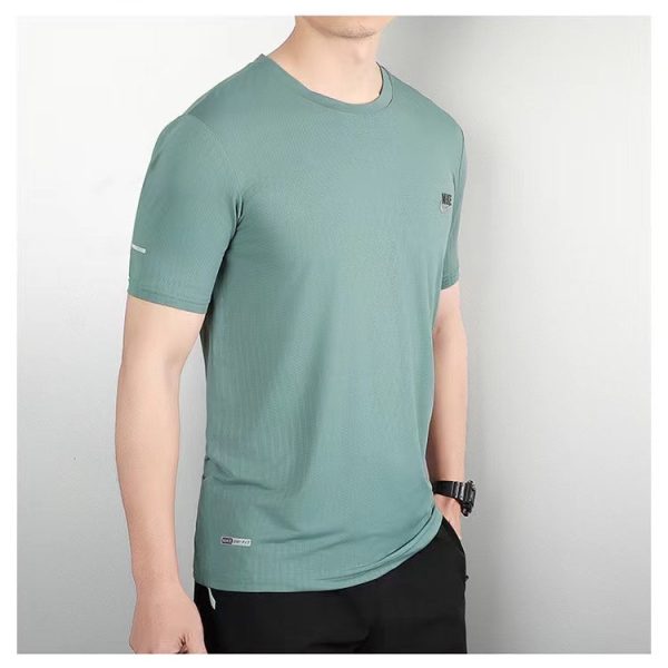 Man wearing teal short-sleeve athletic T-shirt with a small chest logo, standing against a light backdrop.