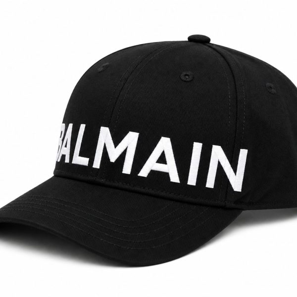 Black baseball cap with a curved brim and a bold white BALMAIN logo across the front.