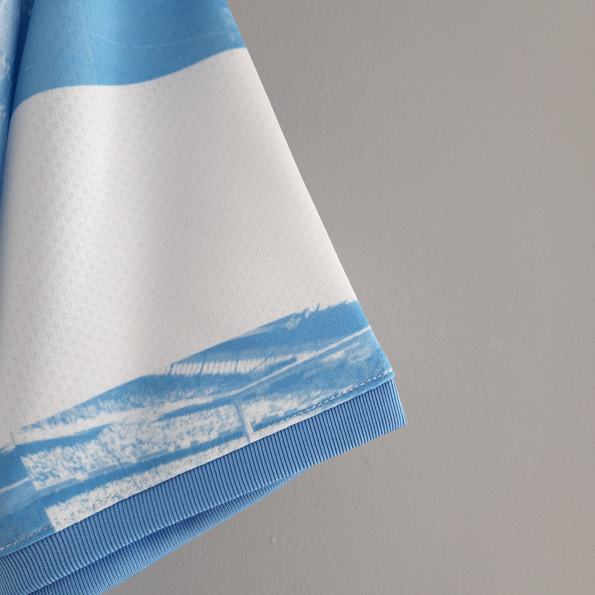 0aa7d4c7_8178f57e-5374-4fb9-895f-11947b1c9bf3 | UAE SPORT STORE Close-up of a light blue and white striped fabric cuff on blue denim, set against a gray background.