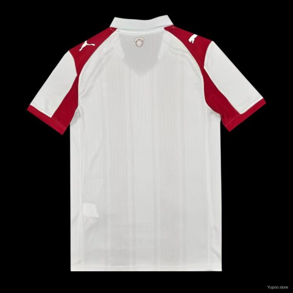 Back view of a white soccer jersey with red shoulder panels and a small crest at the collar on a black background.